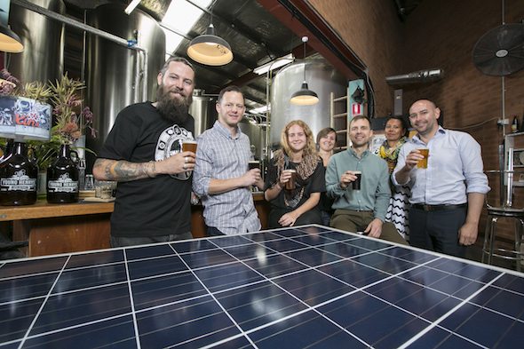 Oscar McMahon (l) of Young Henry’s and members of a communtiy solar project pose for a photograph with a solar panel inside the Young Henry’s brewery. (photo by Jamie Williams/City of Sydney)